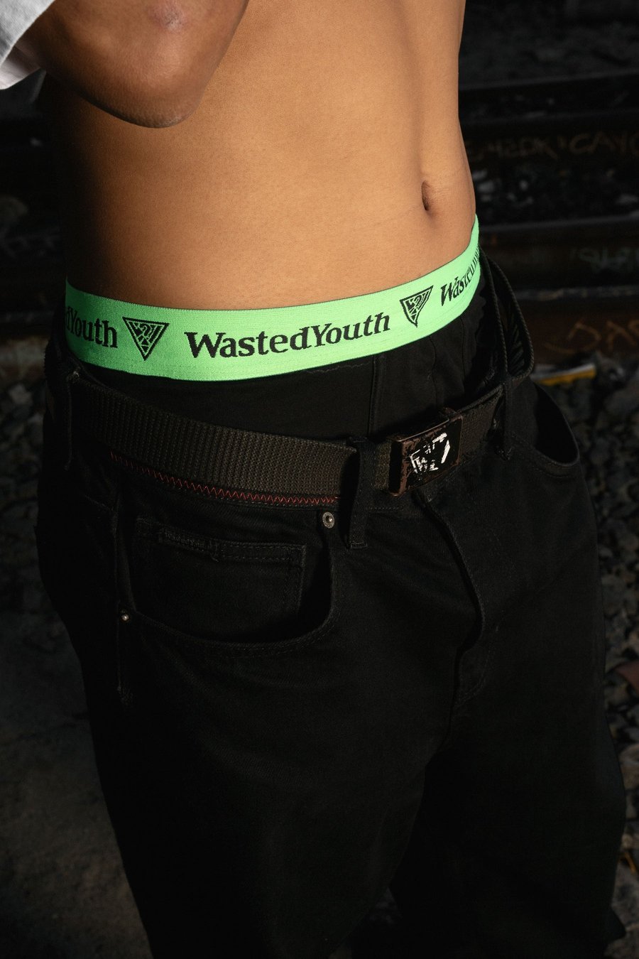 Зелёная резинка боксеров с надписью Wasted Youth над поясом чёрных джинсов
