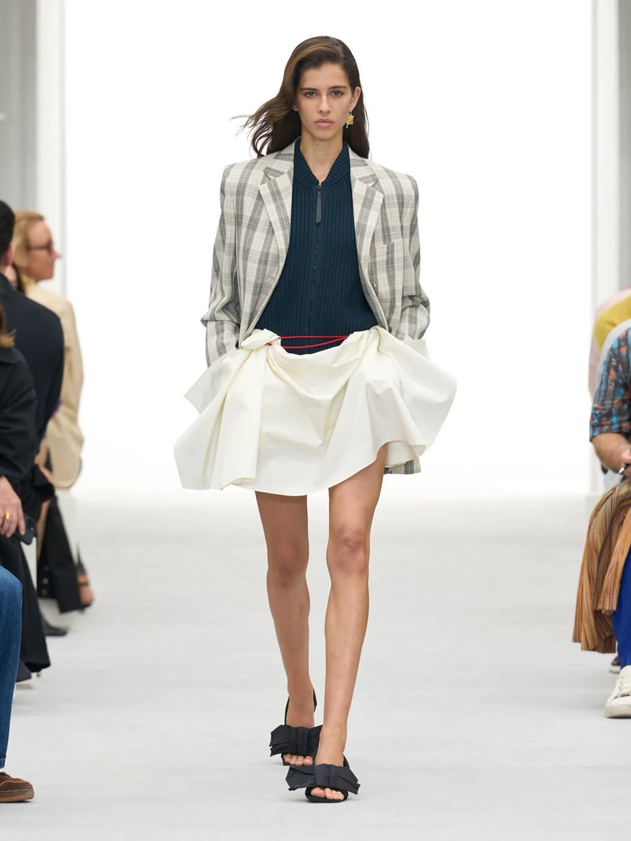 Loewe весна-лето 2027, образ 1: клетчатый пиджак, тёмное поло и белая драпированная мини-юбка