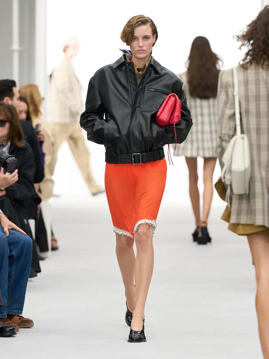Loewe весна-лето 2027, образ 11: чёрная кожаная куртка, оранжевая юбка с бахромой и красная сумка